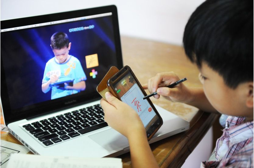 A boy writes a Chinese character on his cellphone as he watches a TV programme called 'hanzi yingxiong', Chinese characters hero, at his home in Beijing on August 23, 2013. AFP PHOTO (Photo credit should read STR/AFP/Getty Images)