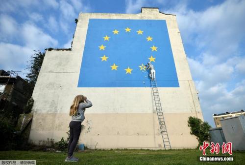 资料图：街头艺术家班克西的画作，画面中一名工人正从欧盟12星旗帜上抹掉一颗星，寓意着英国将脱离欧盟。